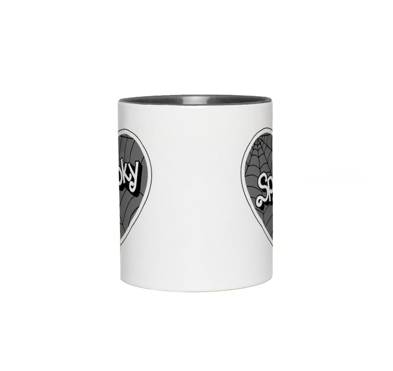 May include: White ceramic mug with a black rim. The mug has a black and white graphic of a heart with a spiderweb and the word "Spooky" on it.