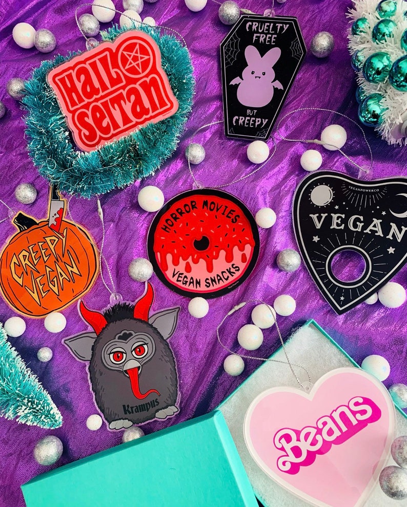 Puede incluir: Una colecci&oacute;n de adornos navide&ntilde;os originales. Incluyen dise&ntilde;os con las frases "Hail Seitan", una calabaza con "Creepy Vegan", una rosquilla con "Horror Movies Vegan Snacks", un ata&uacute;d con un conejito y "Cruelty Free But Creepy", una tabla Ouija con "Vegan", Krampus y un coraz&oacute;n rosa con "Beans".