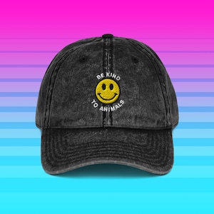 Op de afbeelding: Zwarte baseballpet met een gebogen klep. De pet heeft een gele smiley en de geborduurde tekst "BE KIND TO ANIMALS". De hoed is gemaakt van een gewassen, verweerde stof.