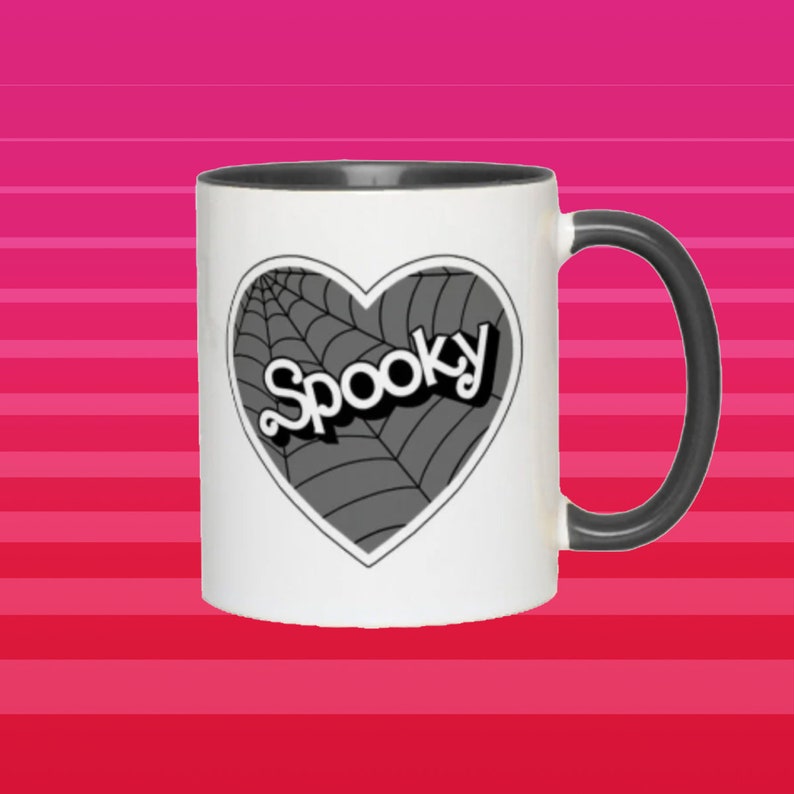 May include: White ceramic mug with a black handle. The mug has a black and white design of a heart with a spiderweb and the word "Spooky" inside.