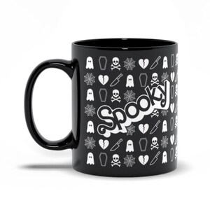 May include: Black ceramic mug with a white "Spooky" text design. The mug is covered in a pattern of white Halloween-themed icons, including ghosts, coffins, spiderwebs, broken hearts, knives, and skulls with crossbones.