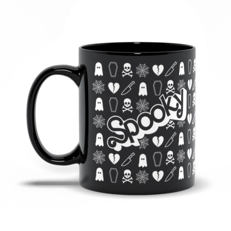 May include: Black ceramic mug with a white "Spooky" text design. The mug is covered in a pattern of white Halloween-themed icons, including ghosts, coffins, spiderwebs, broken hearts, knives, and skulls with crossbones.