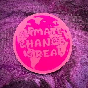 May include: A pink round sticker with a graphic of the Earth and the text "Climate Change Is Real" in a bubble font.