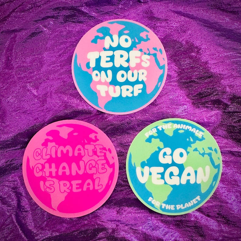 May include: Three round stickers with a globe design. The stickers have different messages: "No Terfs On Our Turf", "Climate Change Is Real", and "For The Animals Go Vegan For The Planet".