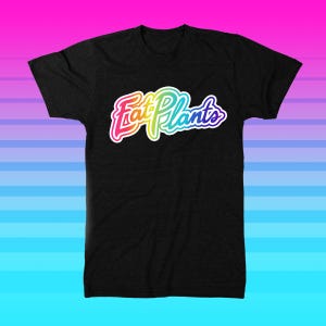 Può includere: Maglietta nera con una grafica arcobaleno che dice "Eat Plants".