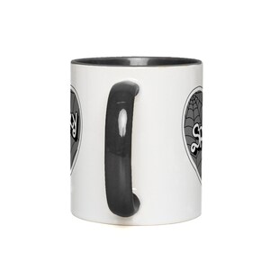 May include: A white ceramic mug with a black rim and handle. The mug has a black and white graphic of a heart with a spiderweb and the word "Spooky" on it.