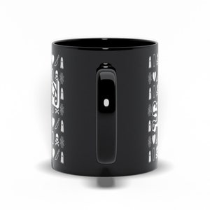 May include: Black ceramic mug with a white Halloween-themed pattern. The design includes ghosts, knives, spiderwebs, and the word "Spooky" in a stylized font. The mug has a black handle and a glossy finish.