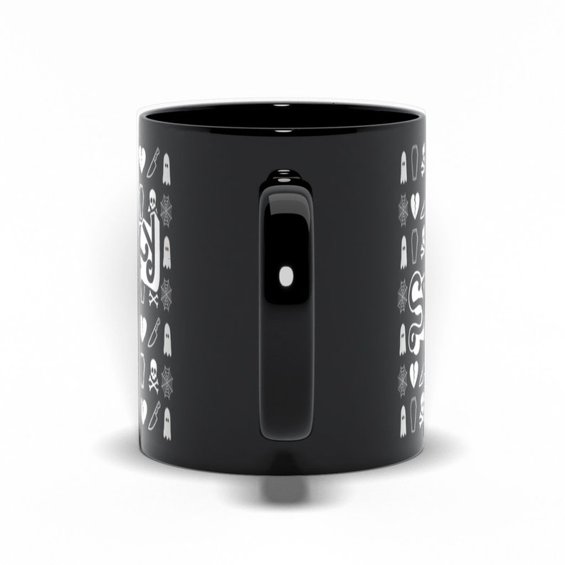 May include: Black ceramic mug with a white Halloween-themed pattern. The design includes ghosts, knives, spiderwebs, and the word "Spooky" in a stylized font. The mug has a black handle and a glossy finish.