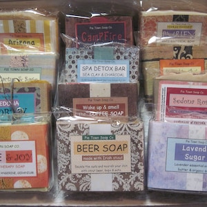 K&ouml;nnte beinhalten: Eine Sammlung von 10 handgefertigten Seifen mit verschiedenen D&uuml;ften und Designs. Die Seifen sind in Klarsichtfolie verpackt und in zwei Reihen angeordnet. Einige der Seifenlabels beinhalten "Arizona", "Campfire", "Spa Detox Bar", "Sedona Vortex", "Love & Joy", "Beer Soap", "Lavender Sugar" und "Sedona Rose".