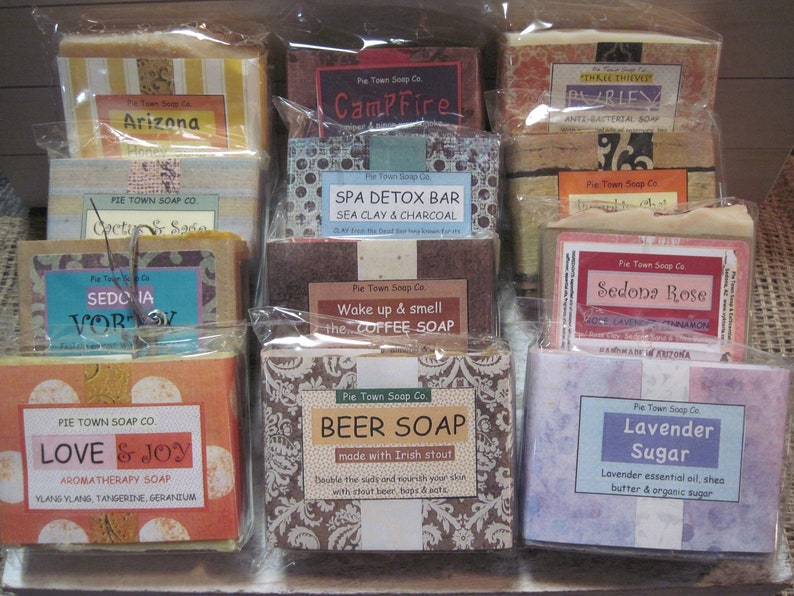 K&ouml;nnte beinhalten: Eine Sammlung von 10 handgefertigten Seifen mit verschiedenen D&uuml;ften und Designs. Die Seifen sind in Klarsichtfolie verpackt und in zwei Reihen angeordnet. Einige der Seifenlabels beinhalten "Arizona", "Campfire", "Spa Detox Bar", "Sedona Vortex", "Love & Joy", "Beer Soap", "Lavender Sugar" und "Sedona Rose".