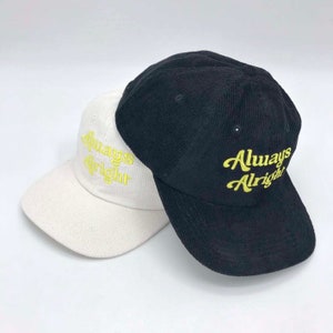 May include: Two corduroy baseball caps, one white and one black, with the text "Always Alright" embroidered in yellow on the front.