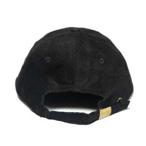 May include: A black corduroy baseball cap with a gold metal buckle closure.