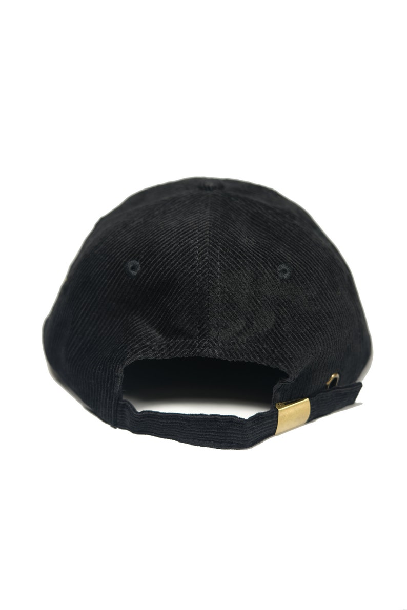 May include: A black corduroy baseball cap with a gold metal buckle closure.