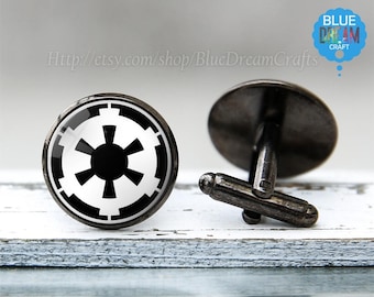 May include: A pair of black cufflinks with a white Imperial symbol from Star Wars. The cufflinks are made of metal and have a round shape.
