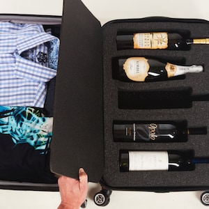 May include: A black suitcase with a built-in wine and champagne carrier. The suitcase is open and the carrier is filled with five bottles of wine and champagne. The suitcase is on a white background.