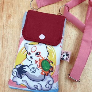 Könnte beinhalten: Eine rosa und weiße Handyhülle mit einem Cartoon-Fuchs-Design. Die Hülle hat eine rote Klappe mit einem Knopfverschluss und einen verstellbaren rosa Gurt. Die Hülle hat ein kleines Etikett mit dem Text "Panda Mind Creations".