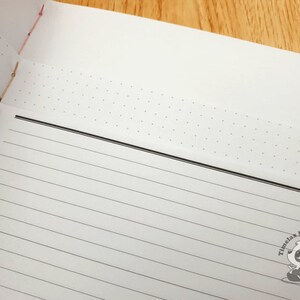 May include: A white notebook with a black line border and a dotted pattern on the top page. The notebook has a black and white panda logo with the text "Timelax Mini Creations".