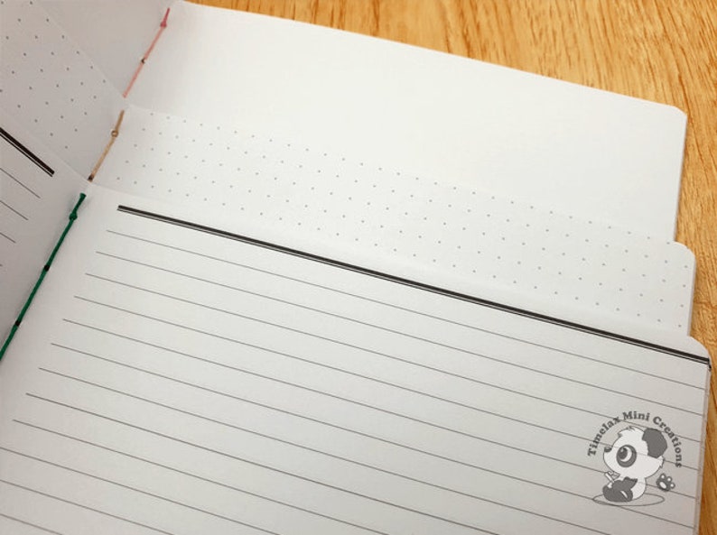 May include: A white notebook with a black line border and a dotted pattern on the top page. The notebook has a black and white panda logo with the text "Timelax Mini Creations".