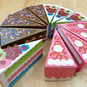 Puede incluir: Un conjunto de 10 rebanadas de pastel de cartón de colores con diferentes diseños. Cada rebanada presenta un sabor de pastel y una cobertura diferentes, que incluyen chocolate, fresa y fruta.