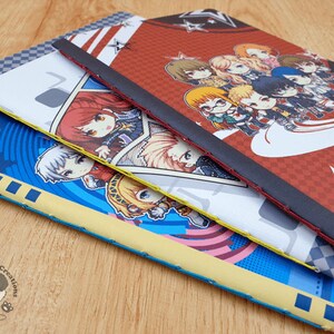 May include: Three different notebooks with colorful covers featuring anime characters. The top notebook has a red and black cover with a group of characters in a star-shaped design. The middle notebook has a white cover with a single character in a blue and white outfit. The bottom notebook has a blue cover with a single character in a yellow and blue outfit.
