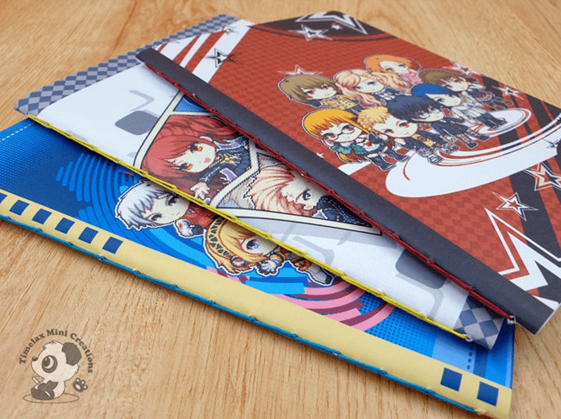 May include: Three different notebooks with colorful covers featuring anime characters. The top notebook has a red and black cover with a group of characters in a star-shaped design. The middle notebook has a white cover with a single character in a blue and white outfit. The bottom notebook has a blue cover with a single character in a yellow and blue outfit.