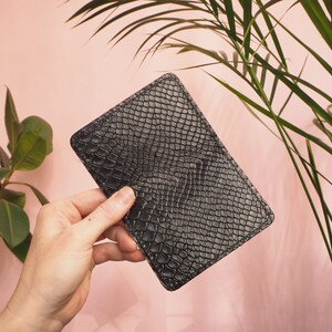 K&ouml;nnte beinhalten: Eine schwarze Lederb&ouml;rse mit Schlangenhautmuster.