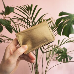 K&ouml;nnte beinhalten: Ein goldfarbener Kartenhalter aus Leder mit einem gen&auml;hten Rand.