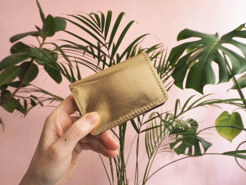 K&ouml;nnte beinhalten: Ein goldfarbener Kartenhalter aus Leder mit einem gen&auml;hten Rand.