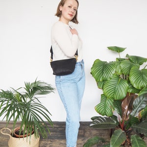 May include: A woman wearing a white sweater, blue jeans, and black sandals. She is carrying a black leather shoulder bag with a gold buckle.