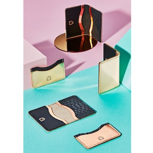 May include: Four different card holders in various colors and materials. The card holders are made of leather and have a gold logo on the front. The card holders are arranged on a pink and blue background.