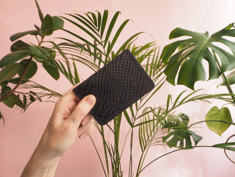 K&ouml;nnte beinhalten: Eine schwarze Lederb&ouml;rse mit strukturierter Oberfl&auml;che. Die B&ouml;rse wird in einer Hand gehalten.