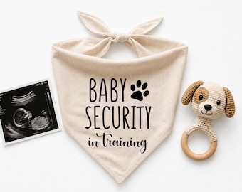 Pode incluir: Uma bandana triangular bege para animais de estimação com o texto preto "BABY SECURITY in Training" e uma pata, acompanhada por uma ecografia a preto e branco e um chocalho de cão em croché com um anel de madeira.