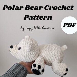 May include: A white crochet polar bear with black paw pads and facial features. The image includes the text "Polar Bear Crochet Pattern" and "By Loopy Little Creatures". The pattern is available as a PDF.