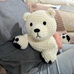 Könnte beinhalten: Ein handgehäkelter, weißer Bär mit schwarzen Augen, Nase und Pfoten. Der Bär ist aus weichem Garn gefertigt. Ein kuscheliges Spielzeug oder ein dekorativer Artikel, ideal für Kinder.