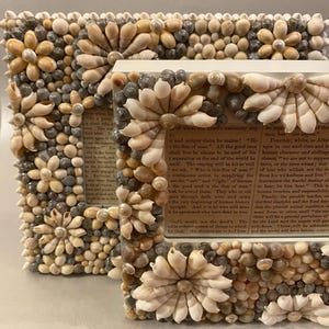 May include: Two white picture frames decorated with seashells. The frames are different sizes and are both standing upright. The smaller frame has a text excerpt visible inside. The text reads: "...and unique claim he makes! "He is the Son of man." All the good men shall live he claims to be need of his separation at the end of the world he himself. The reaping will be his as well we ask, "Who is this Son of man" ..."