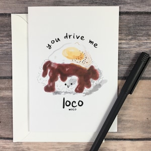 May include: A white card with a cartoon illustration of a plate of rice, gravy, and a fried egg. The text "you drive me loco" is written above the plate and "loco moco" is written below the plate.