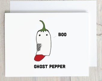 May include: A white greeting card featuring a cartoon illustration of a pepper wearing a white ghost costume with two black eyes and a red tongue. The text BOO is printed next to the pepper, and the text GHOST PEPPER is printed below it.
