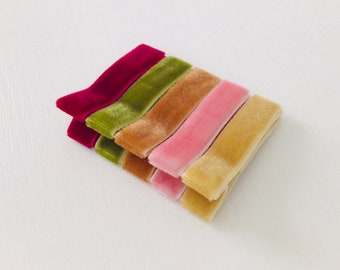 May include: A stack of six velvet ribbon strips in various colors, including burgundy, green, brown, pink, and gold.