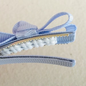 May include: A light blue hair clip with a bow. The clip has a metal base with a textured grip and a light blue ribbon bow.