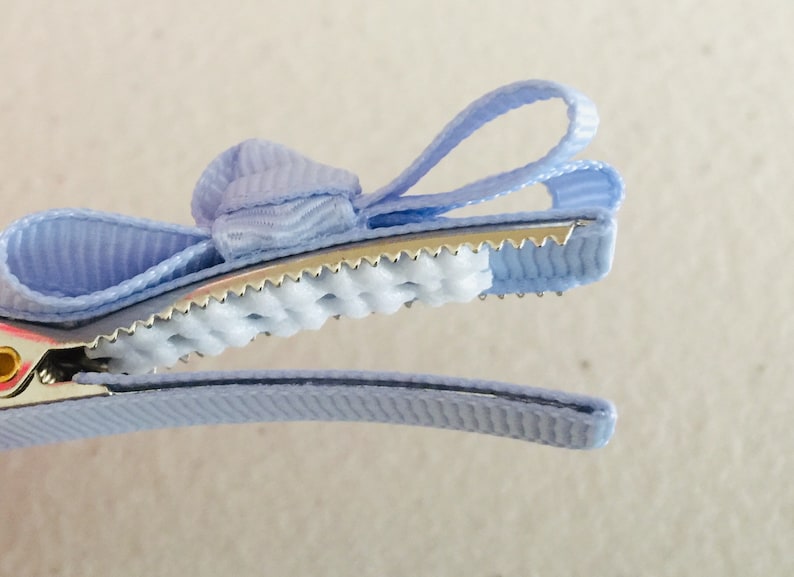 May include: A light blue hair clip with a bow. The clip has a metal base with a textured grip and a light blue ribbon bow.
