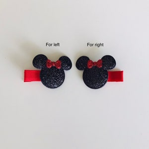 May include: Two black glitter Minnie Mouse hair clips with red bows. The clips are attached to red ribbon.