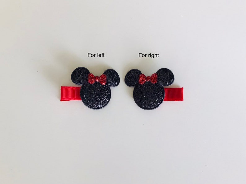 May include: Two black glitter Minnie Mouse hair clips with red bows. The clips are attached to red ribbon.