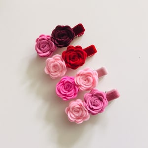May include: Set of six felt flower hair clips in shades of pink and red. Each clip features a single or double flower with a velvet backing.