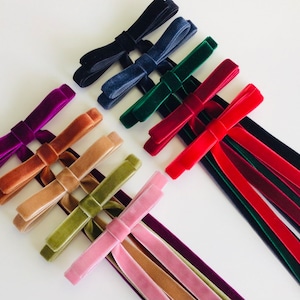 May include: Assortment of velvet ribbon bows in various colors, including purple, brown, beige, green, pink, navy, dark green, and red. The ribbons are tied into bows with long tails.