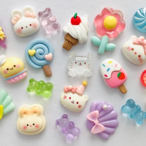 Peut inclure: Une collection de breloques miniatures en r&eacute;sine color&eacute;e de diff&eacute;rentes formes, dont des sucettes, des lapins, des ours, des cornets de glace, des fleurs et des cerises. Les breloques pr&eacute;sentent des couleurs pastel et des motifs mignons de style dessin anim&eacute;.