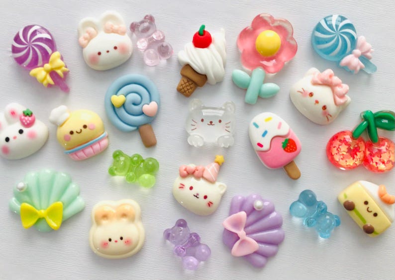 Peut inclure: Une collection de breloques miniatures en r&eacute;sine color&eacute;e de diff&eacute;rentes formes, dont des sucettes, des lapins, des ours, des cornets de glace, des fleurs et des cerises. Les breloques pr&eacute;sentent des couleurs pastel et des motifs mignons de style dessin anim&eacute;.
