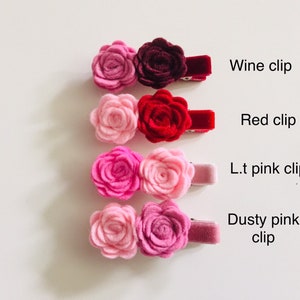 May include: Four pairs of felt flower hair clips in various shades of pink and red. The clips are arranged vertically from darkest to lightest, with the top clip labeled "Wine clip", the second clip labeled "Red clip", the third clip labeled "L.t. pink clip", and the bottom clip labeled "Dusty pink clip".