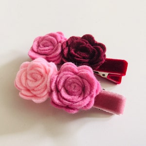 May include: Three felt flower hair clips in shades of pink and burgundy. The flowers are attached to velvet covered alligator clips.