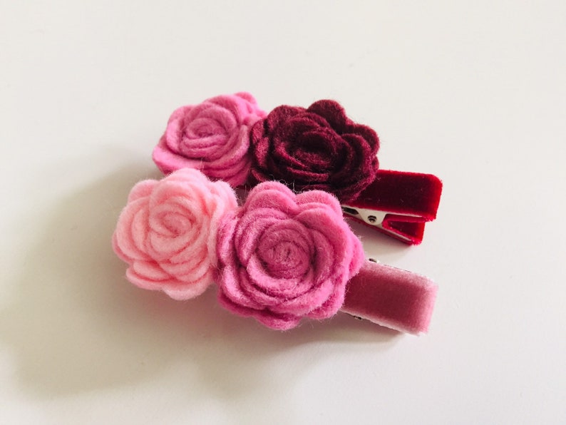 May include: Three felt flower hair clips in shades of pink and burgundy. The flowers are attached to velvet covered alligator clips.