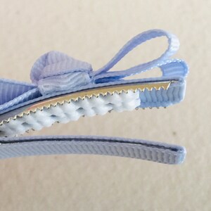 May include: A light blue hair clip with a bow. The clip has a textured grip and a metal spring.